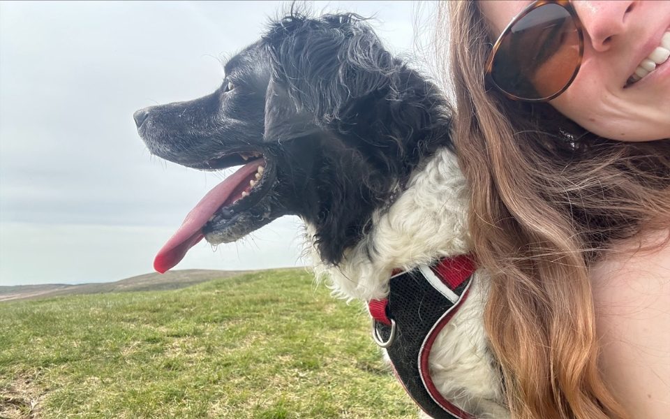 Joni Franieczek talking a selfie with her black and white dog in a field.