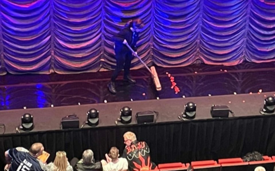 Joni Franieczek sweeping confetti onstage in front of a gold curtain.