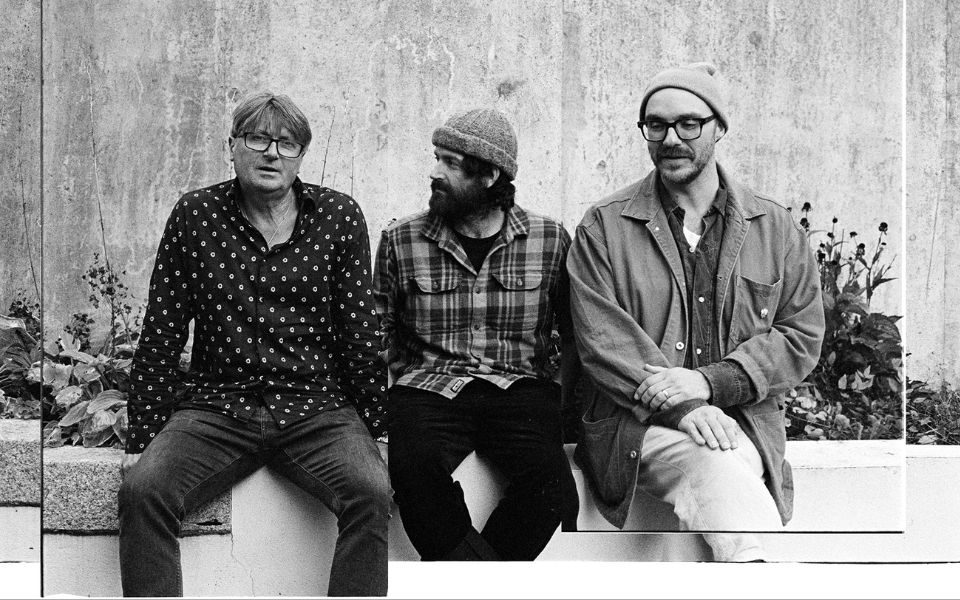 Black and white, textured, collage-style image of the three members of LYR sitting candidly on a brick wall.