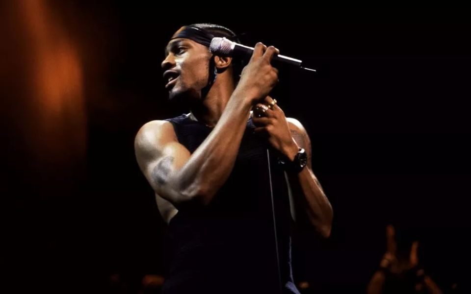 D'Angelo holds a microphone and looks to a crowd off-stage.