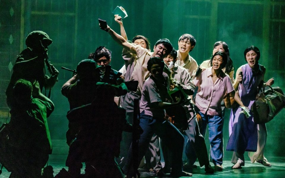 A group of people desperately crying and shouting at soldiers holding guns. The civilians carry luggage and brandish documents, trying to get past.