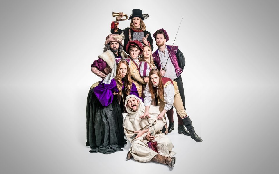 A group of characters in Shakespearean costumes huddle together and pose with quizzical expressions against a blank background.