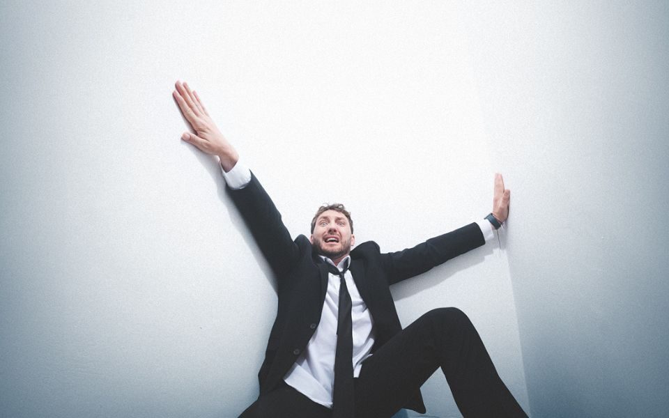 Looking panicked in the corner of a white room, Seann Walsh holds onto the walls with stretched arms and legs.
