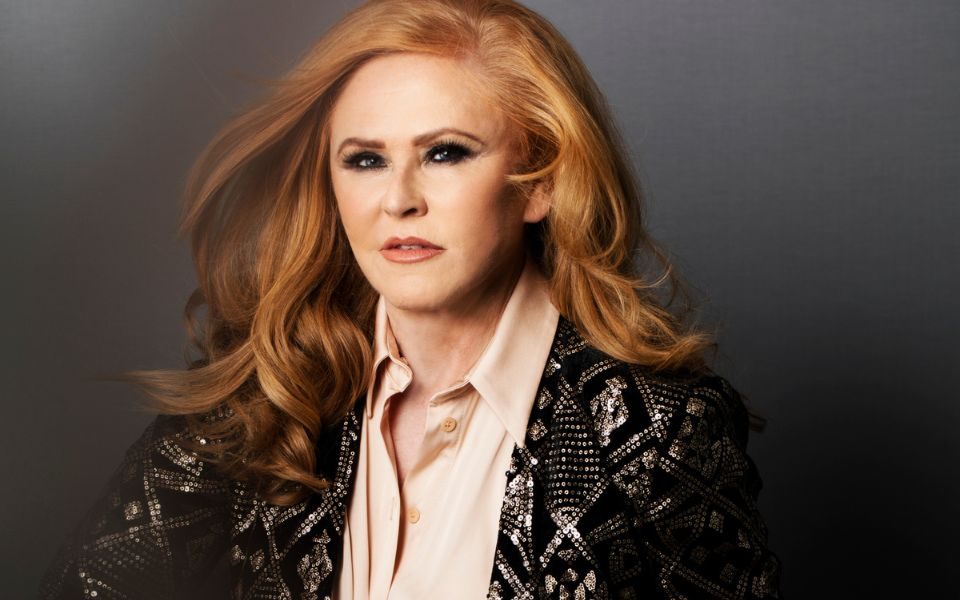 Carol Decker poses in a decorative jacket with windswept hair blowing over her shoulder.