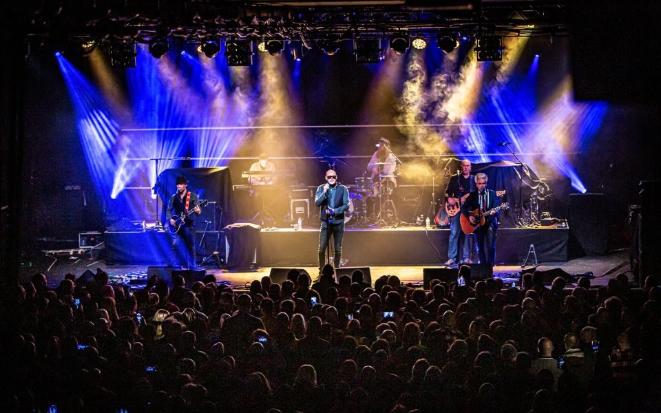 The Christians perform onstage to a packed crowd, lit by blue and yellow spotlights.