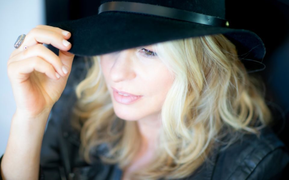 Vonda Shepard lightly tips the brim of her black hat, from a candid camera angle.