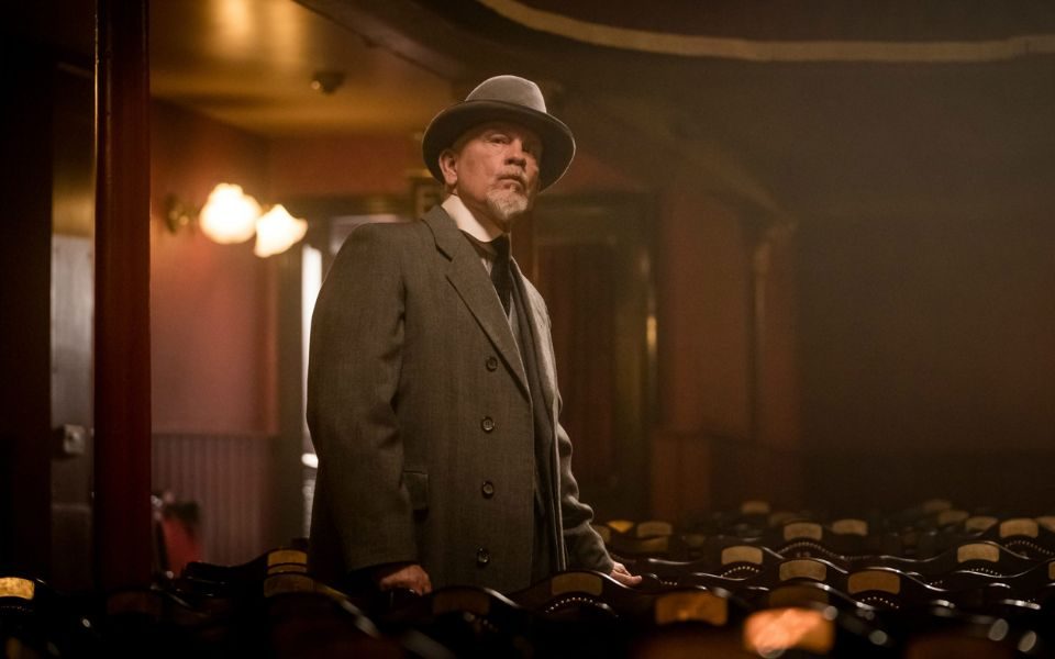 John Malkovich peruses the City Varieties Music Hall auditorium with a white goatee and apprehensive gaze.