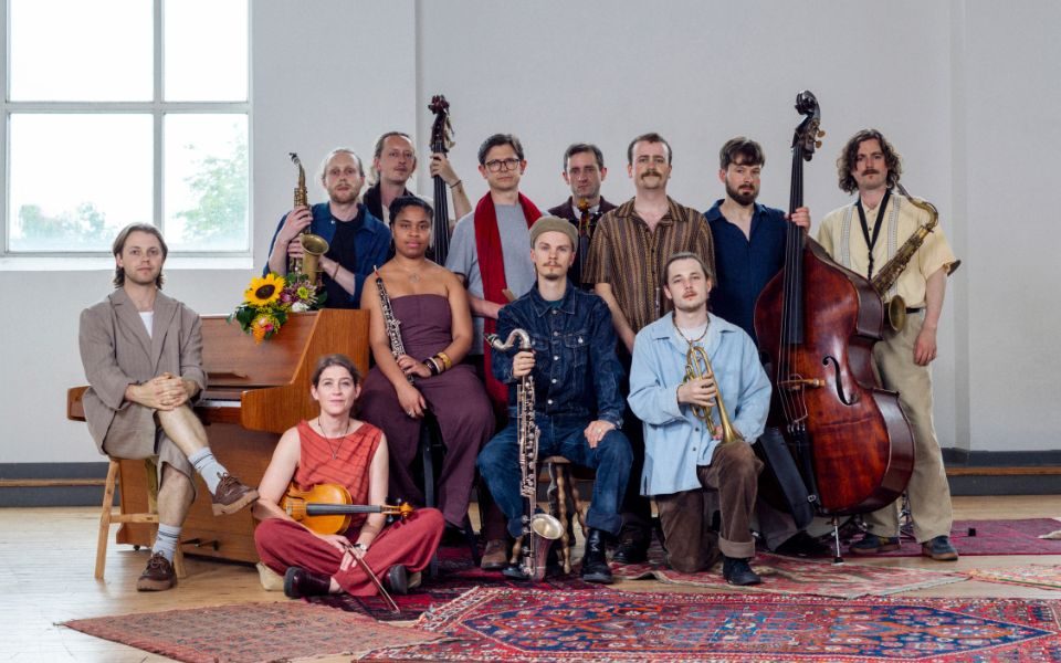 The Ancient Infinity Orchestra lined up and holding their respective instruments in a bright room laden with rugs.