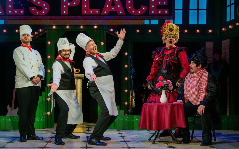 A scene from Aladdin: The Rock 'n' Roll Panto, with three characters posing in chef uniforms, as the Dame and Villain react.