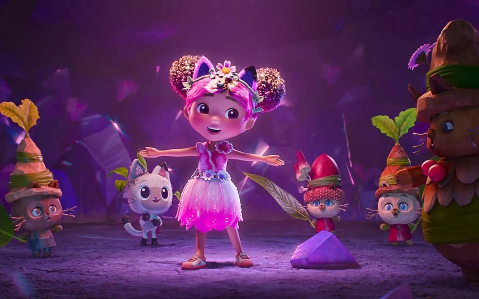 Digital animated still. A girl in a pink dress and floral accessories smiles, surrounded by cats wearing foliage and leafy hats.