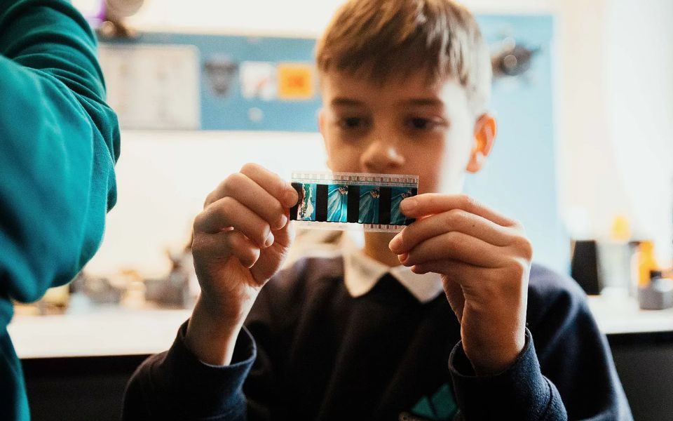 A child examines a short reel of celluloid film print in his hands.