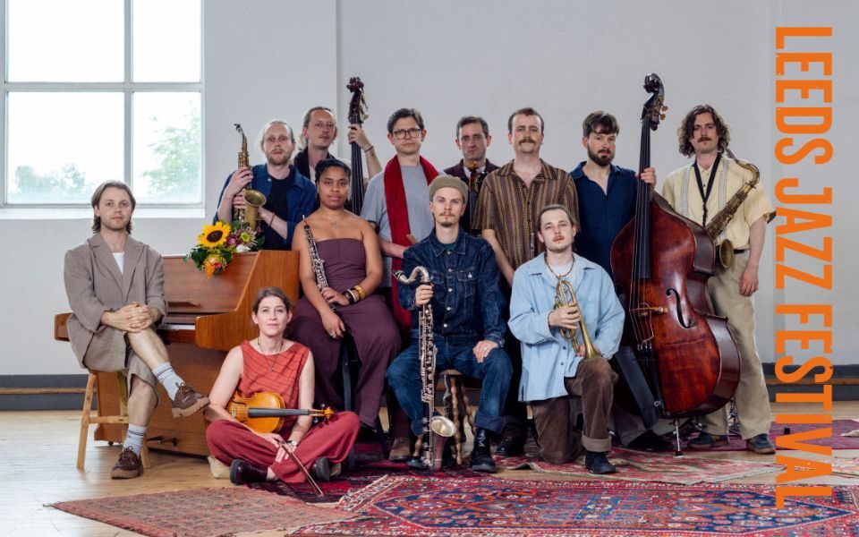 The Ancient Infinity Orchestra lined up and holding their respective instruments in a bright room laden with rugs.