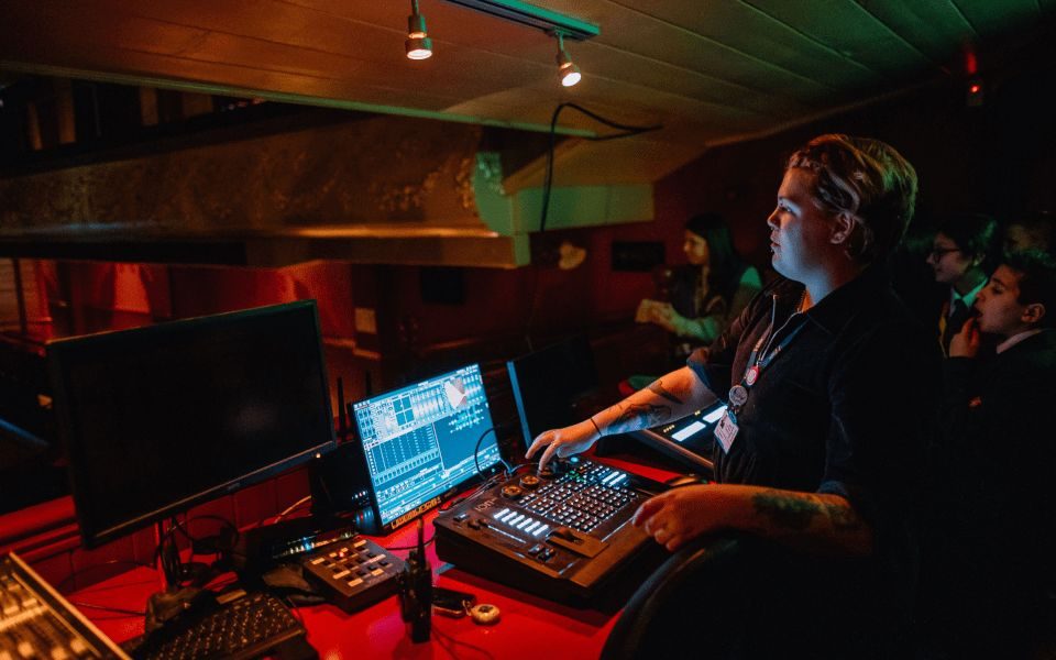 A member of the technical team is giving a demonstration to young people on the lighting desk at City Varieties