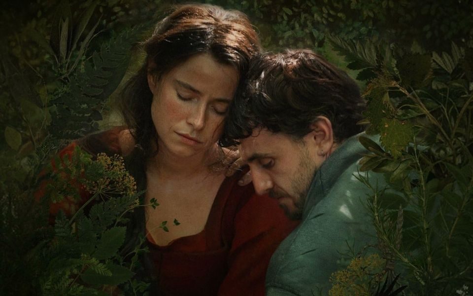 Jessie Buckley and Paul Mescal with eyes closed, resting their heads against each other and framed by foliage.