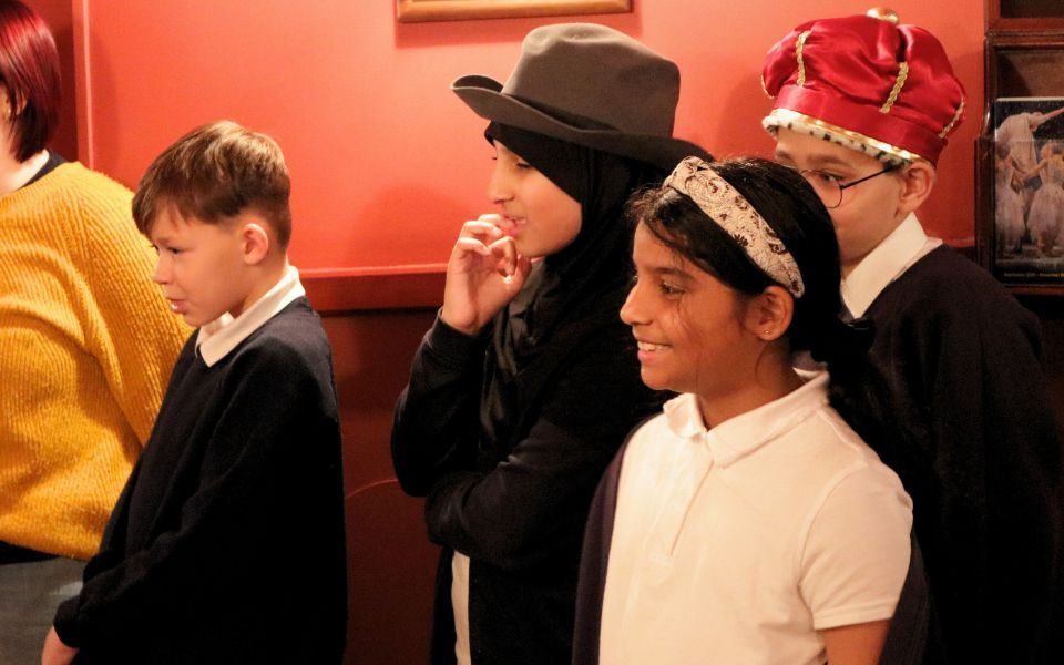 Students smiling in the corridors of Leeds Grand Theatre wearing costume hats.