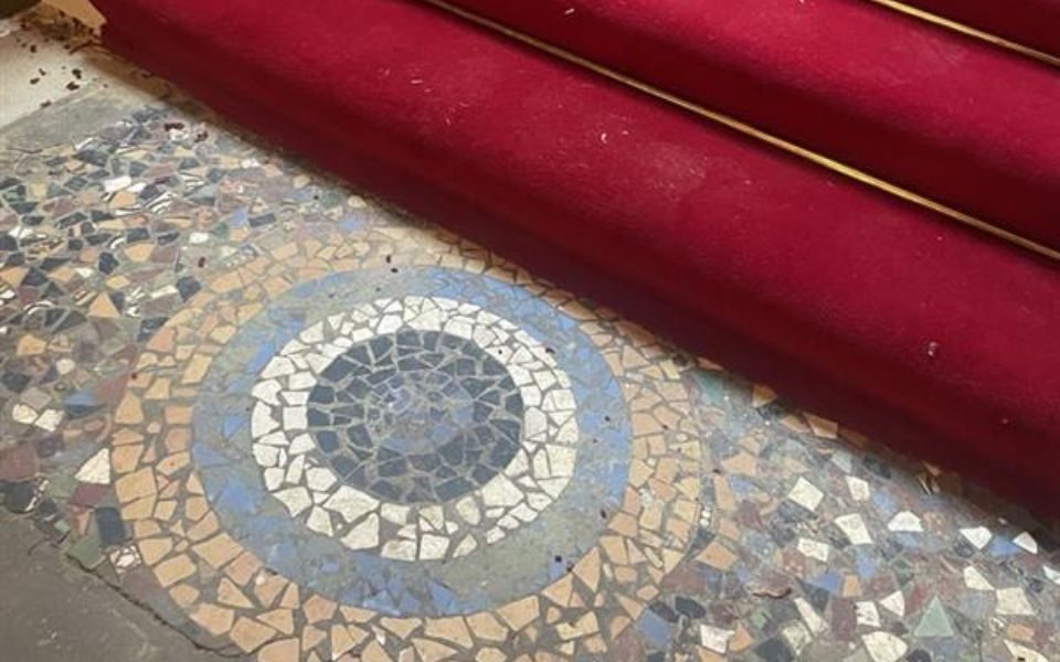 Ornate tiles in a circular pattern at the bottom of a red-carpeted staircase.