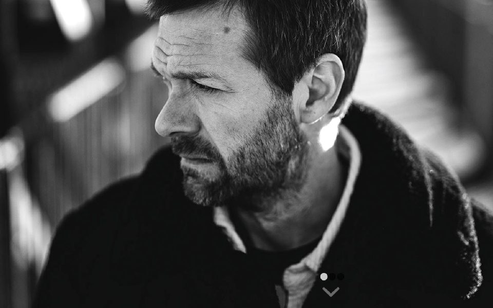 Black and white photo of Tom Meighan looking off into the distance, wearing a thick coat.