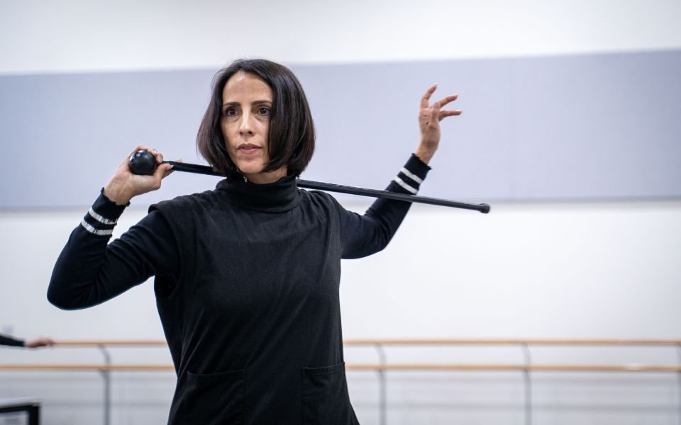 Annabelle Lopez Ochoa dressed in black and holding a cane over her shoulders in the Northern Ballet rehearsal studio.