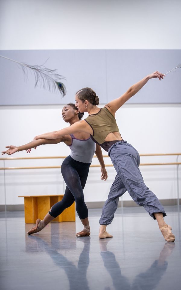 Gemma Coutts and Aerys Merrill dancing together with their arms elegantly outstretched in the rehearsal studio.