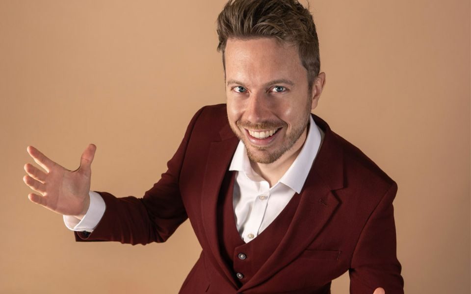 James B Partridge smiles in a maroon suit, with arms open.