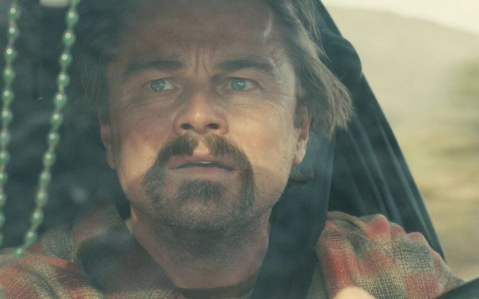 Leonardo DiCaprio looking dishevelled and stressed in a driver's seat, seen through the car windscreen.