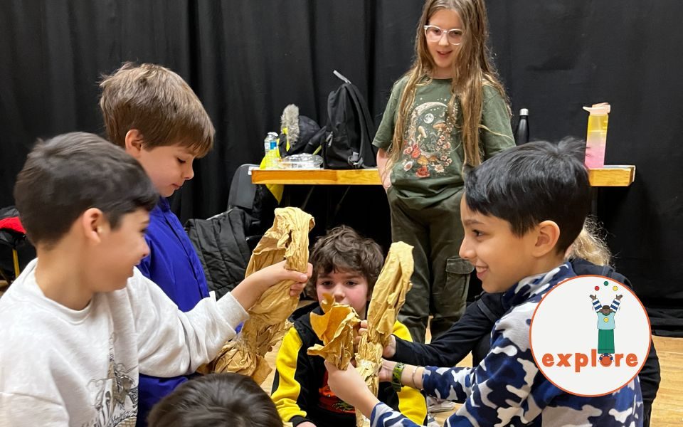 A group of young people sit in a circle, making something with paper. In the bottom right corner, a roundel featuring a playful illustration of a person juggling stood on the word 'explore'.