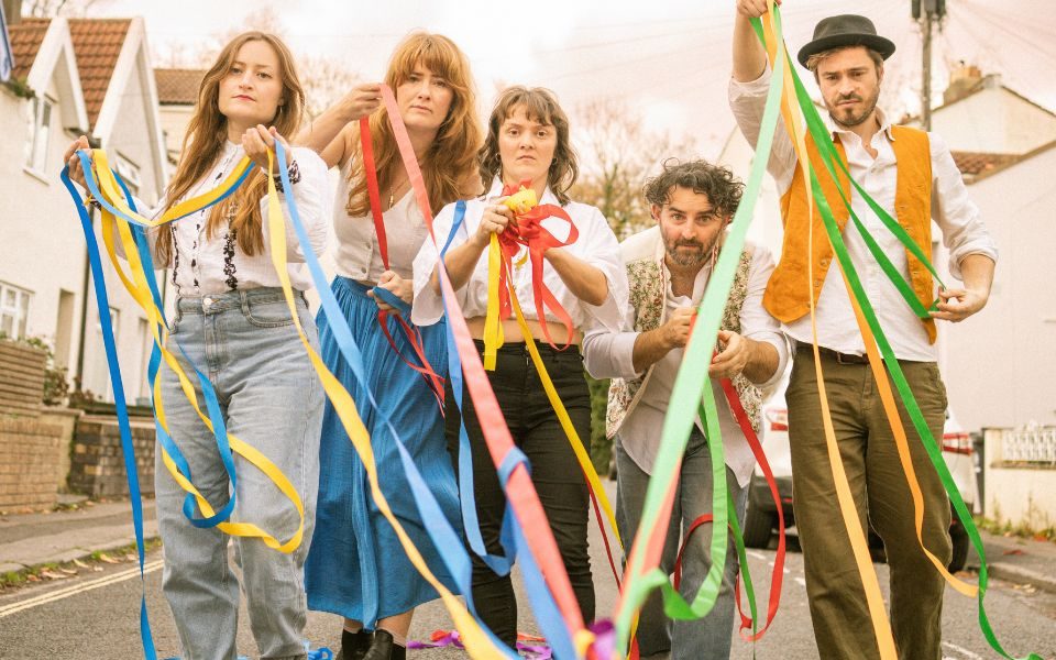The members of Wakefire walk through a sunny street with colourful ribbons.