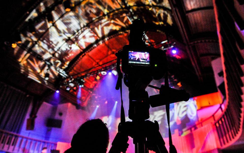 A camera, with Howard Assembly Room lit in bright colours out of focus in the background.