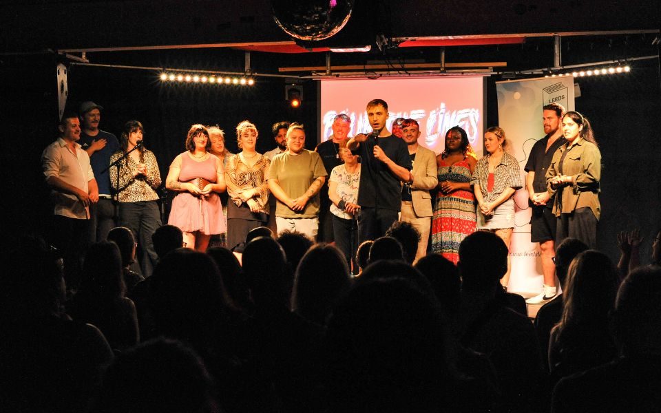 A group of people stood on stage together as Lence speaks into a microphone at Blur the Lines