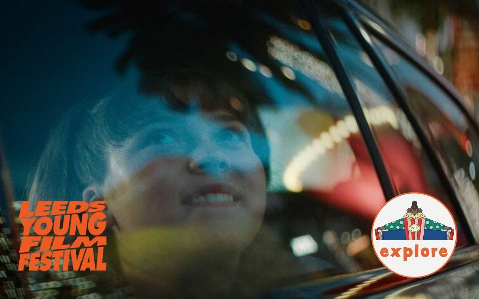 A smiling child gazes through a car window, which reflects trees and lights. In the bottom left, an orange logo reading 'Leeds Young Film Festival'. In the bottom right corner, a roundel featuring a playful illustration of a person sat peering over a bucket of popcorn, on the word 'explore'.