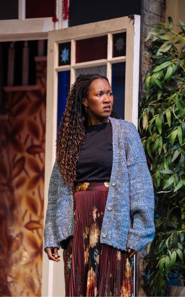 Shvorne Marks as Jenny, looking worried and wearing a cosy oversized cardigan.