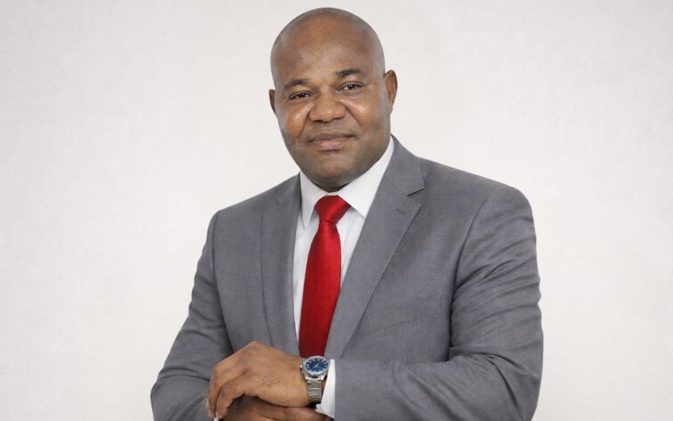 Headshot of Innocent Igiehon in a grey suit and red tie, folding his arms with a subtle smile.
