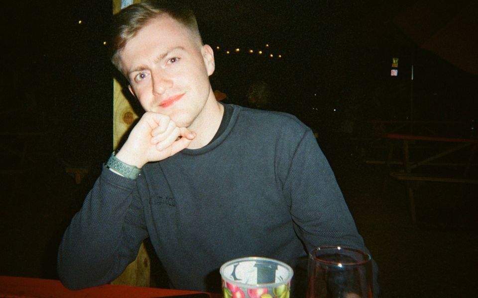 On a bench at night, Kieron Ferries smiles at the camera, resting his head on his hand.