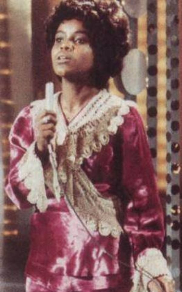 PP Arnold in a purple dress with lace frills, singing into a 1960s-era microphone.