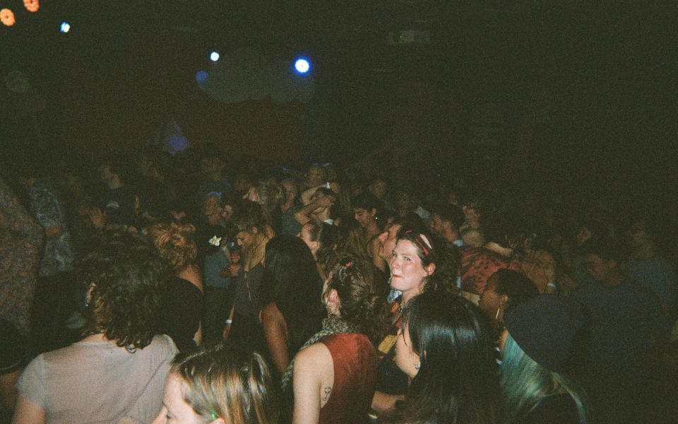 In low light, a packed crowd of audience members look up towards a stage off-camera.