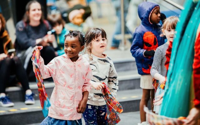 Two children wave patterned pieces of fabric as part of a crowd in a busy market.