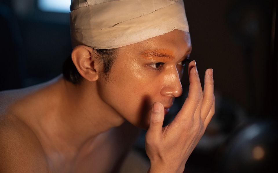 A person applies make-up to their eyebrows with their finger and their head is taped.