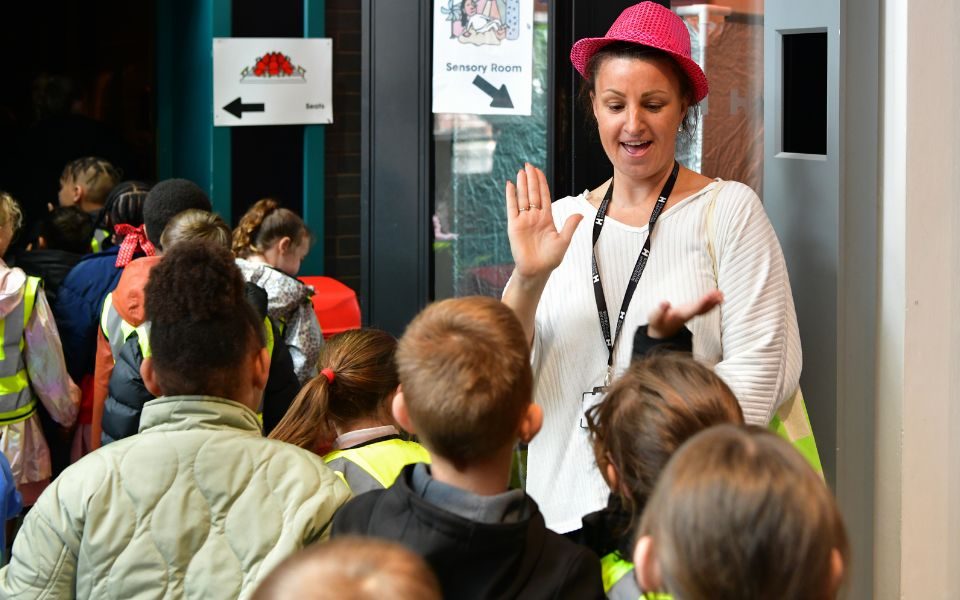Someone in a pink hat holds a hand up towards a group of children.