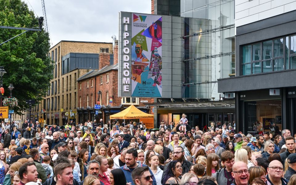 A busy crowd of people outside Birmingham Hippodrome. The sign shows a poster for Birmingham Weekender.