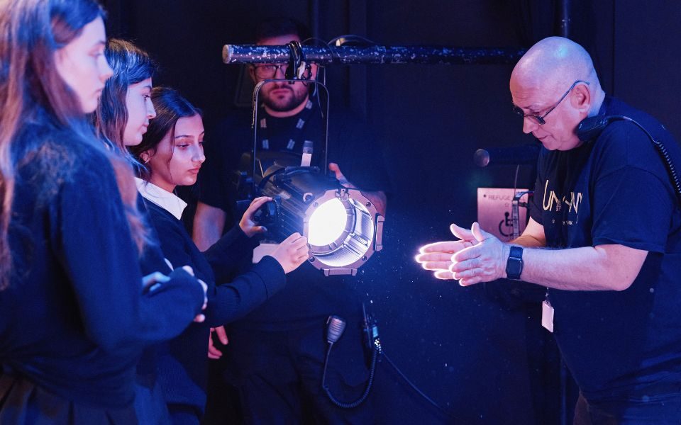 Children in school uniform hold a spotlight while a technician teaches them about it.