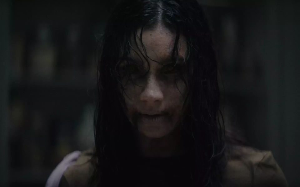 In dark, shadowy lighting, the face of a girl with dark, wet hair, and dark eyes masked by dirt and make-up.