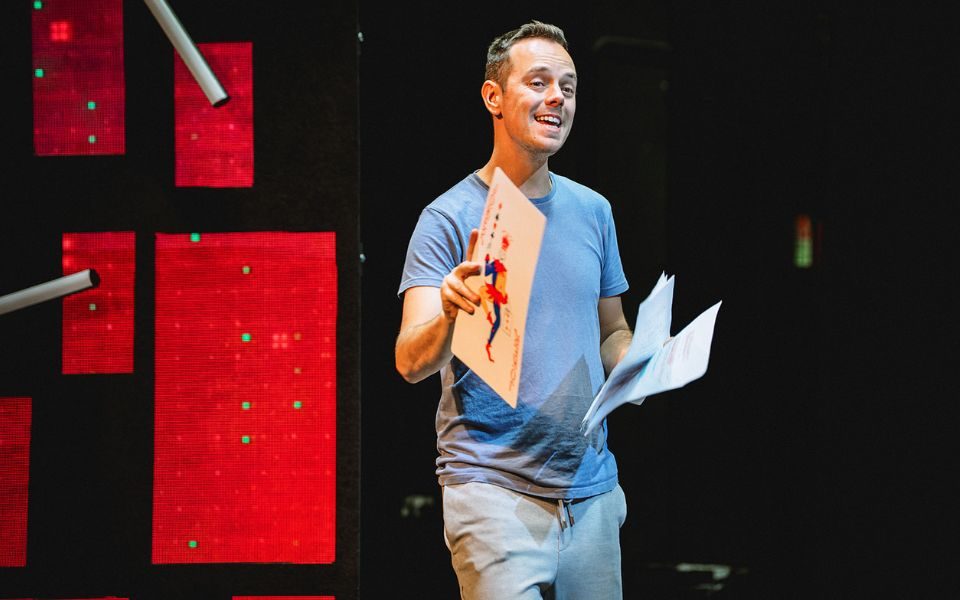 Jamie Docherty holding a giant playing card in one hand and a script in the other.