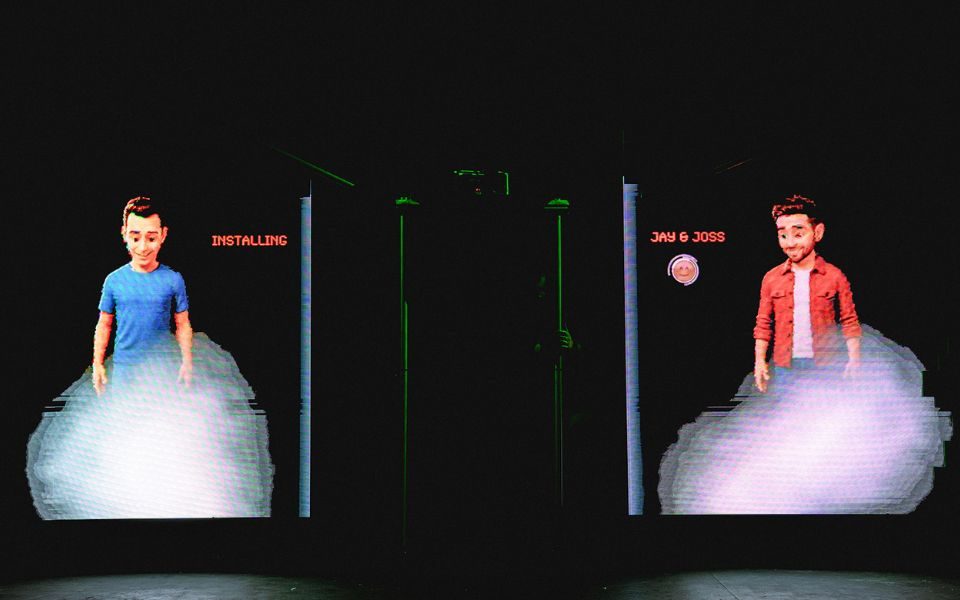 Two video game figures projected onto a wall. One is a man in a blue top with text reading 'Installing' next to him. The other is a man in a red jacket with text reading 'Jay & Joss' next to him and a smiley face.