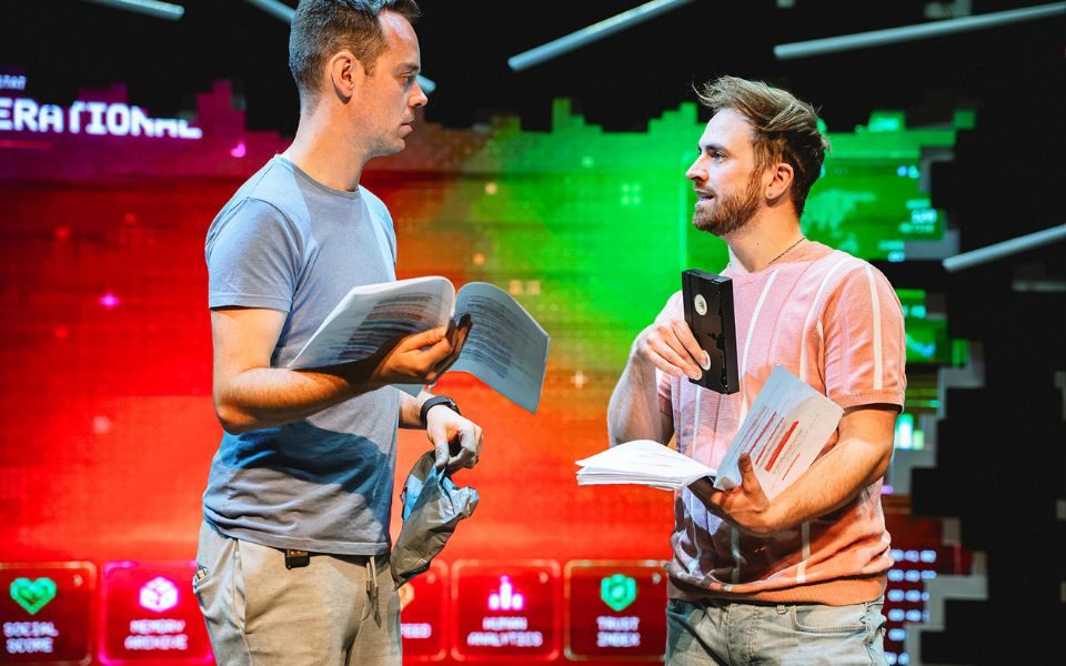 Jay and Joss face each other talking with scripts in their hands. Joss holds a video tape in his other hand.