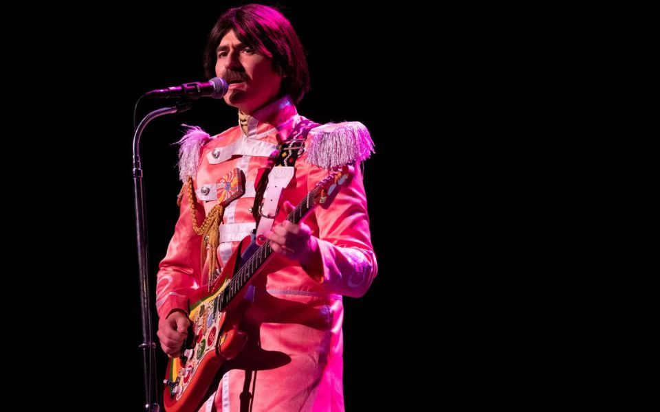 A musician performs as George Harrison in a classic Sgt. Pepper's Lonely Hearts Club Band costume