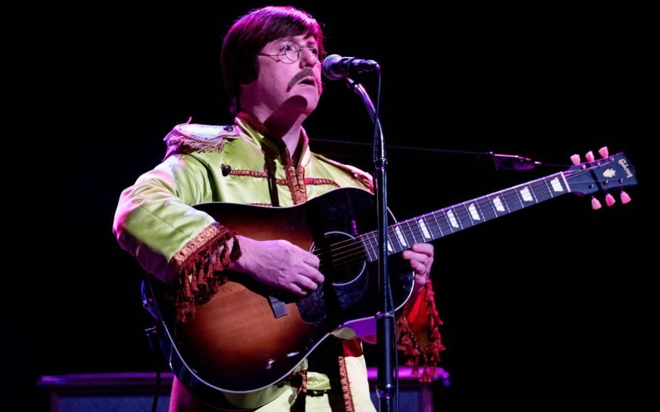 A musician performs as John Lennon in a classic Sgt. Pepper's Lonely Hearts Club Band costume
