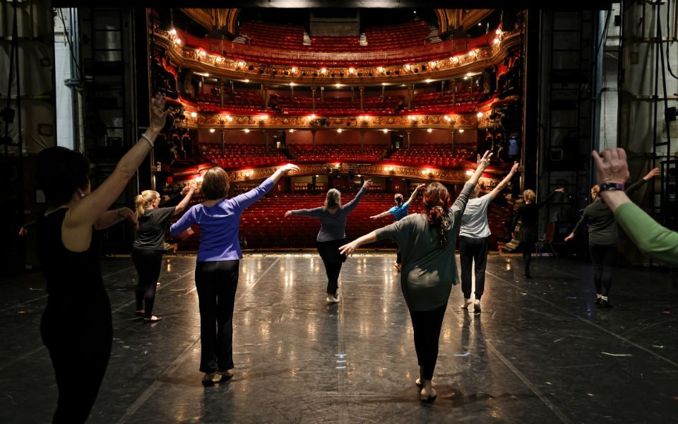 On stage in the Leeds Grand Theatre auditorium, a group of people perform ballet poses.