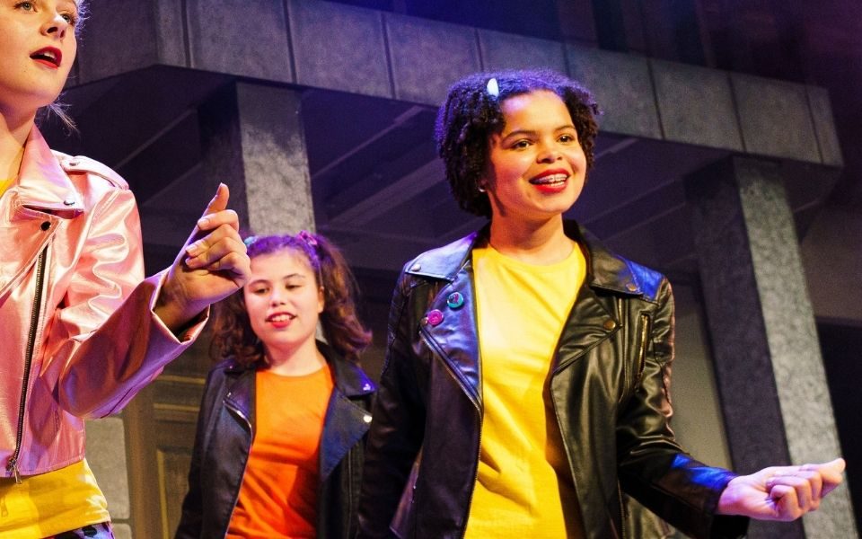 A young person on stage in a leather jacket, dancing