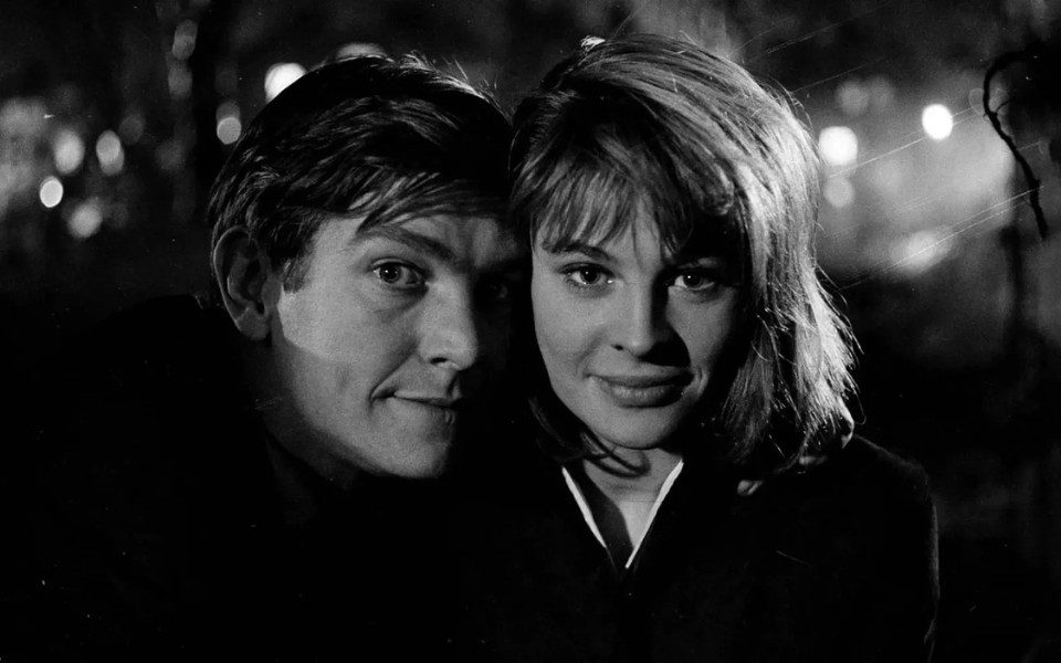 Black and white close-up of Tom Courtenay and Julie Christie smiling at the camera, close to each other.
