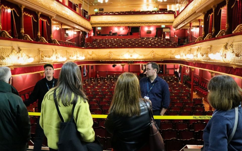 Two staff members in lanyards talk to a group of people on stage in an empty auditorium.